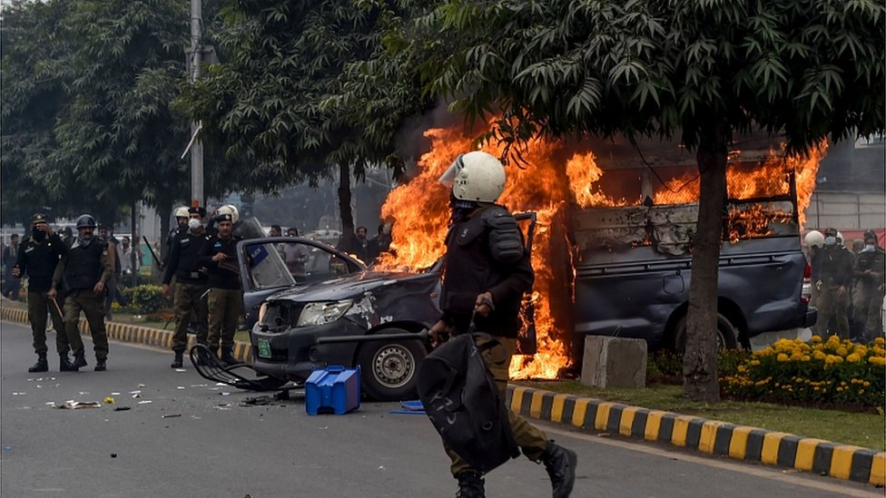 Police gather beside a burning police vehicle following a clash between lawyers and doctors in Lahore on December 11, 2019