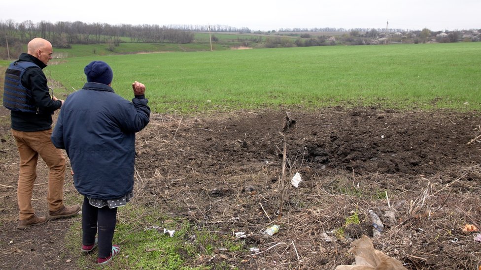 A woman looks at a bomb crater near her home in Avdiivka