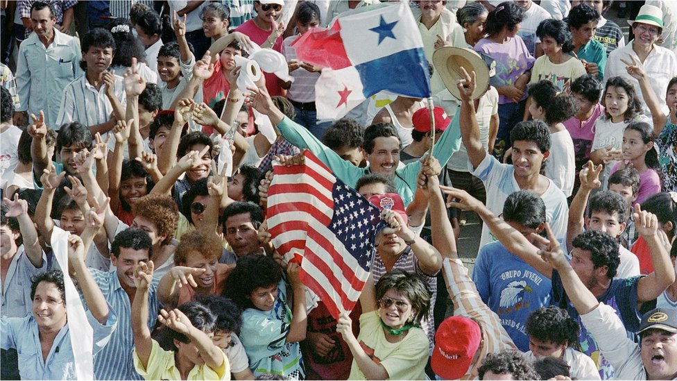 Большое количество панамцев, выступающих против генерала Мануэля Антонио Норьеги, размахивают американскими и панамскими флагами у военного поста 22 декабря 1989 г.