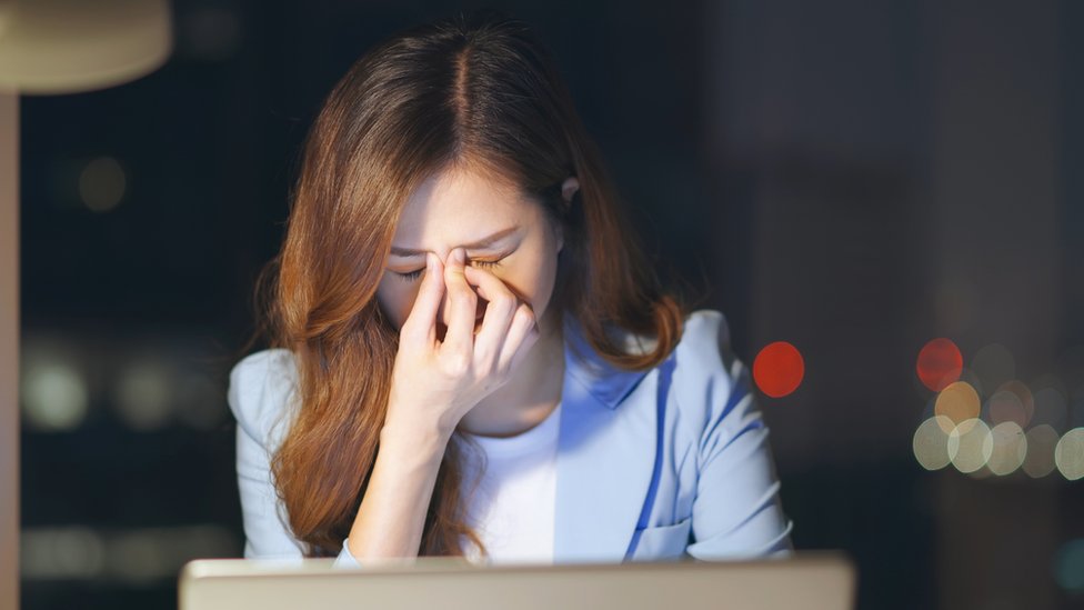 Una mujer con los ojos cansados por la pantalla del computador.