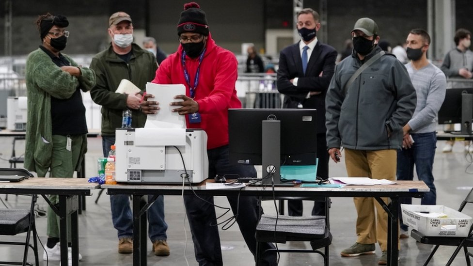 2021年1月5日，佐治亞州亞特蘭大市佐治亞世界會議中心，富爾頓縣的一名選舉工作者在選舉觀察員注視下，將缺席選票放入掃描儀中。