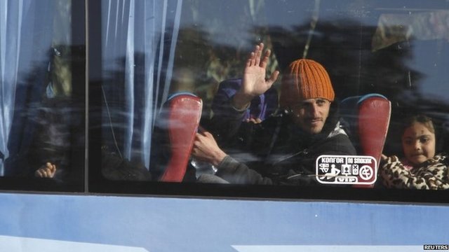 A man waves from the window of a bus