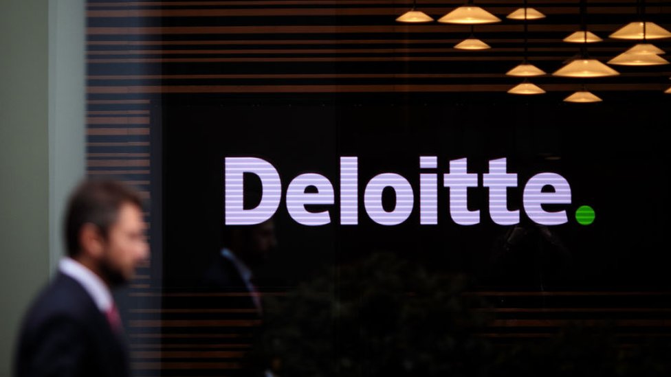 Анонимный мужчина в костюме проходит мимо офиса Deloitte в Лондоне, Великобритания.