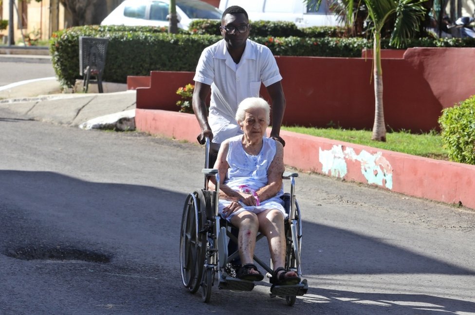 Trabajador de la salud lleva a una mujer en silla de ruedas en un hospital de La Habana.