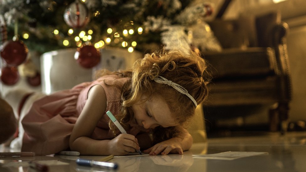criança desenhando com árvore de Natal ao fundo