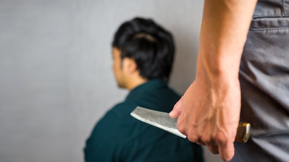 Hombre sosteniendo cuchillo frente a hombre organizado.