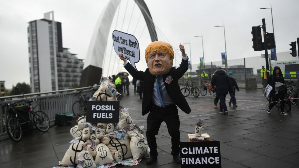 Un manifestante con una máscara del primer ministro Boris Johnson sostiene un cartel que dice "¡Carbón, coches, dinero y sordidez!".