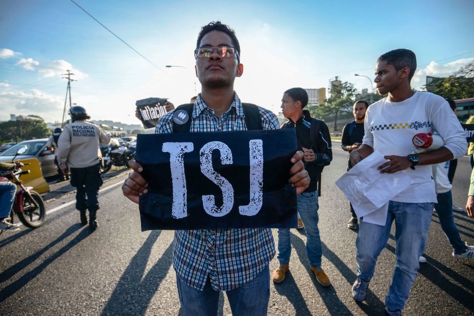 El Tribunal Supremo de Justicia se adjudicó los poderes de la Asamblea Nacional, lo que devolvió al organismo al centro de la polémica. Joven con un cartel que dice TSJ protesta en Caracas, Venezuela.