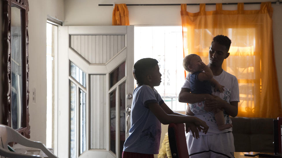 Муж и сын лидера лиги Эйдавис Монтес заботятся о ее ребенке в гостиной ее дома.