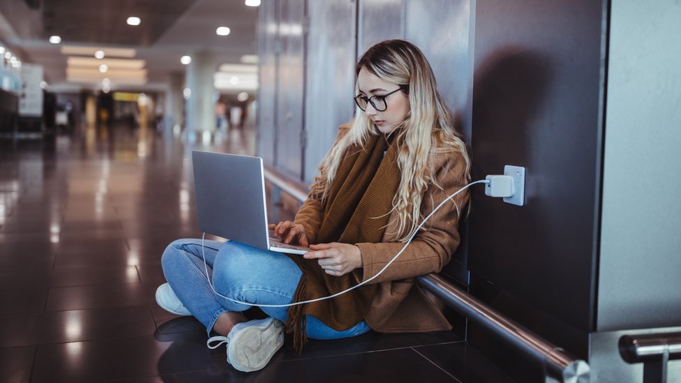 Una joven sentada en el suelo con una laptop enchufada