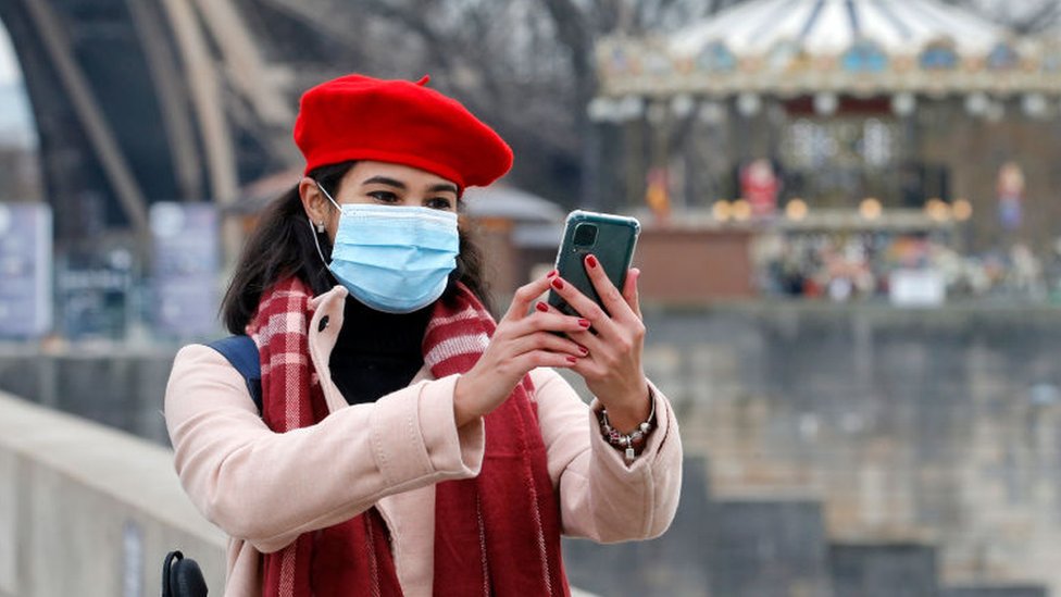 A woman wearing a protective face mask takes a selfie in front of the Eiffel Tower in December