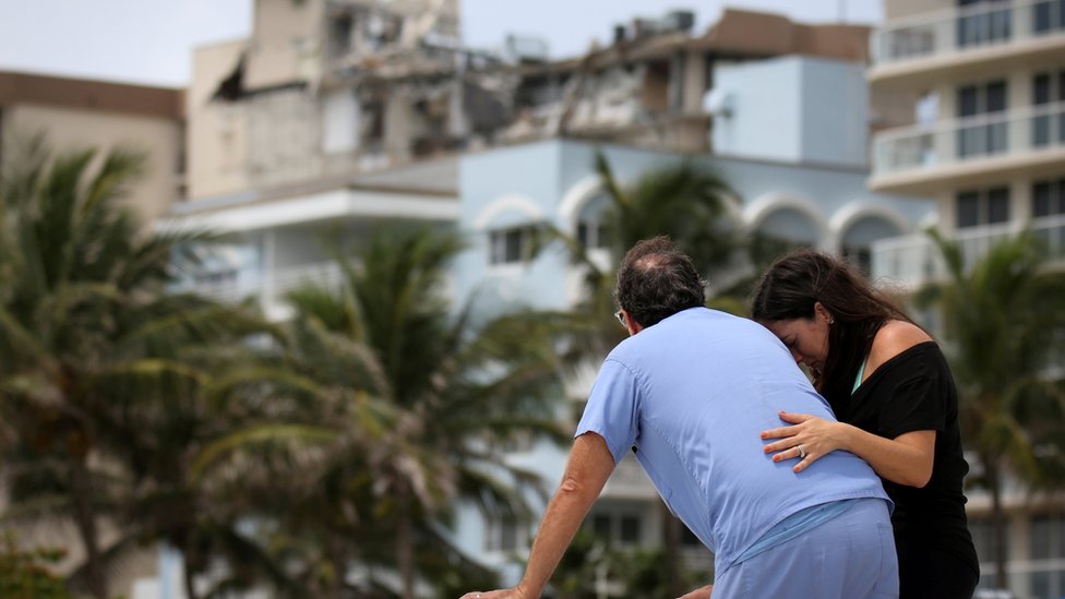 A couple at the beach reacts near the partially collapsed residential building as the emergency crews continue search and rescue operations for survivors, in Surfside, near Miami Beach, Florida, U.S. June 26, 2021