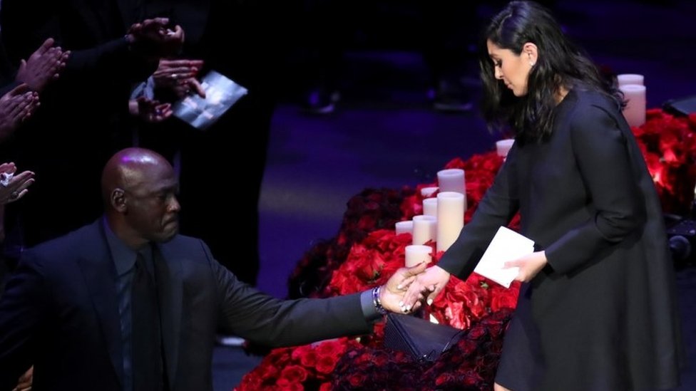 Бывший баскетболист Майкл Джордан помогает Ванессе Брайант покинуть сцену во время публичной церемонии поминовения ее покойного мужа