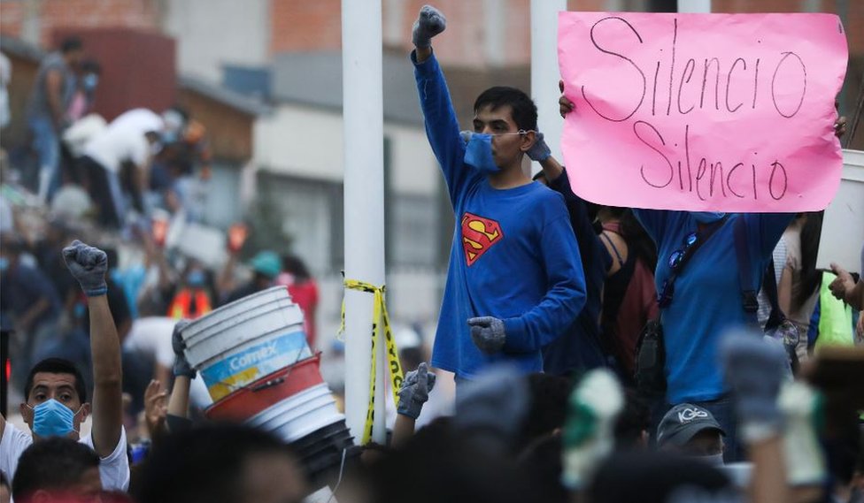 Мальчик в футболке с суперменом поднимает кулак в знак тишины, пока спасатели ищут захороненных жертв землетрясения