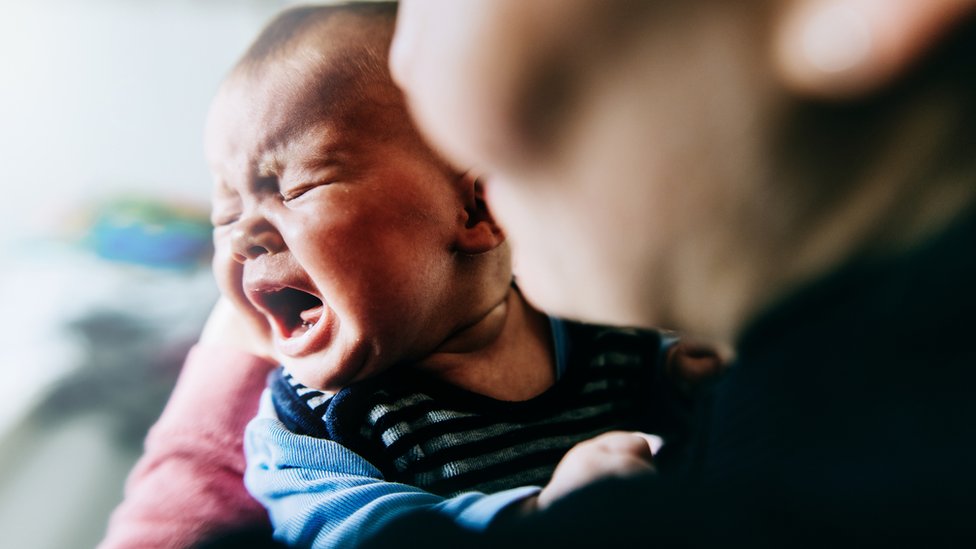 Bebê chorando no colo de mulher