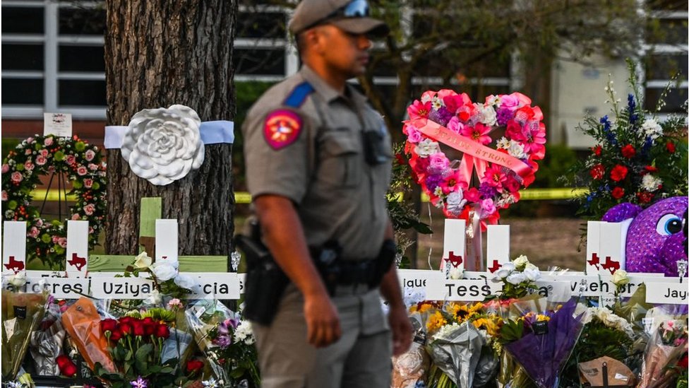 Policía frente a cruces de homenaje a los muertos en el tiroteo de la escuela de Uvalde, Texas.