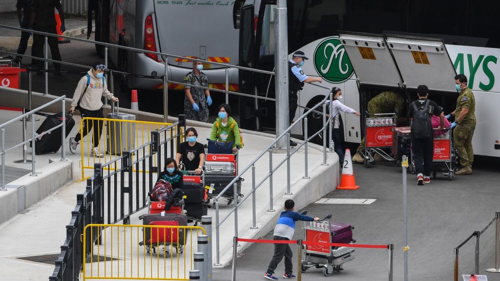 Недавно вернувшиеся пассажиры в масках отправляют свой багаж в карантинный отель в Сиднее