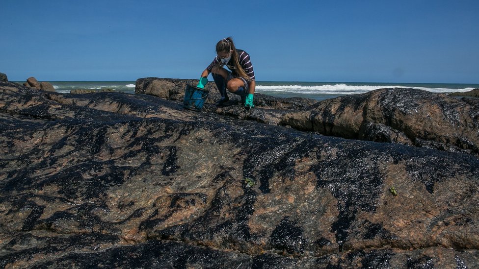 Волонтер очищает от нефти камни на пляже Педра-ду-Сал в Сальвадоре