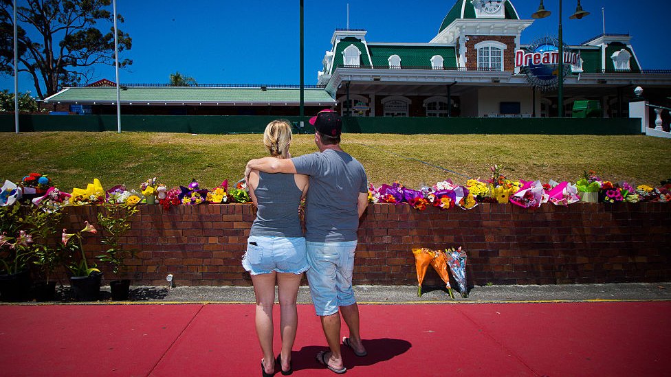 Пара стоит перед цветами возле Dreamworld после аварии в 2016 году