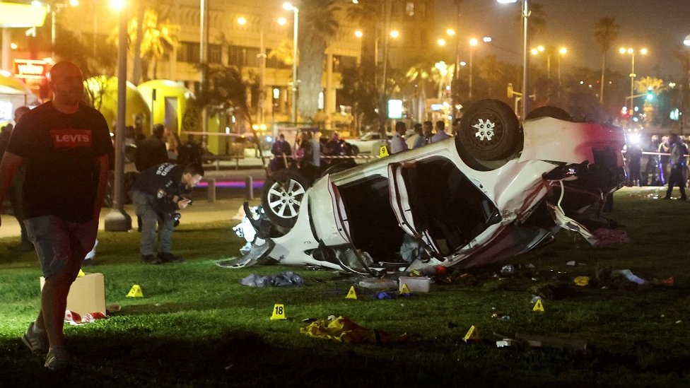 The aftermath of a car ramming attack on the beachside promenade in Tel Aviv. A white car can be seen on its roof.