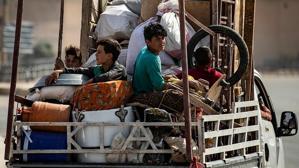 Перемещенные сирийцы сидят в кузове грузовика, в то время как арабские и курдские мирные жители бегут из-за военного нападения Турции на контролируемые курдами районы на северо-востоке Сирии, 11 октября 2019 года в сирийском пограничном городе Таль-Абьяд