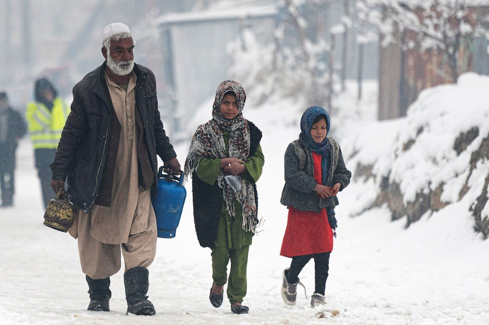 رجل يحمل عبوتا غاز يسير بجوار أطفال على طول أحد الشوارع أثناء تساقط الثلوج في كابل في 11 يناير/كانون الثاني 2023