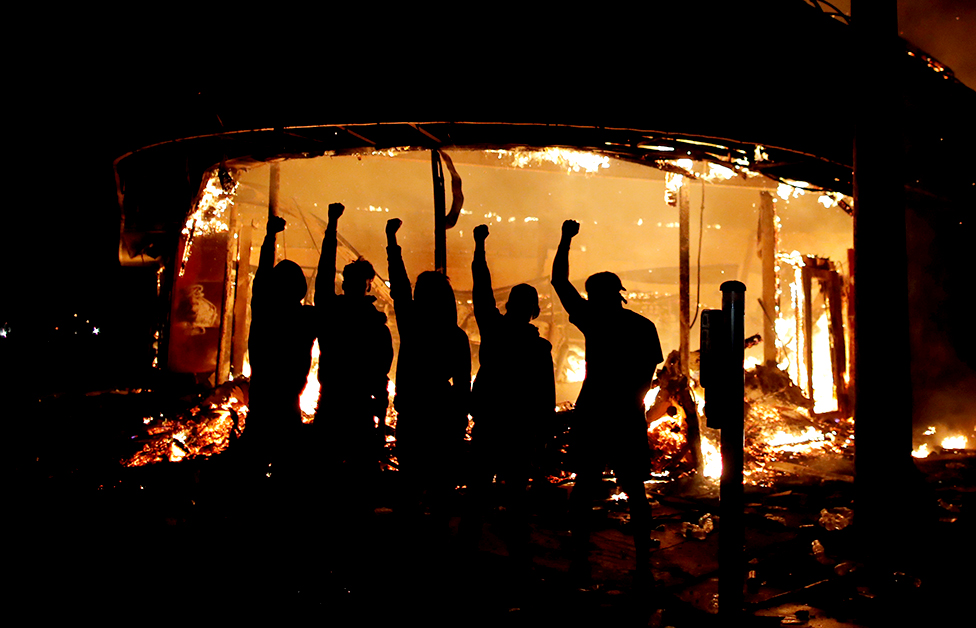 Protesters are seen outside of a liquor store on fire
