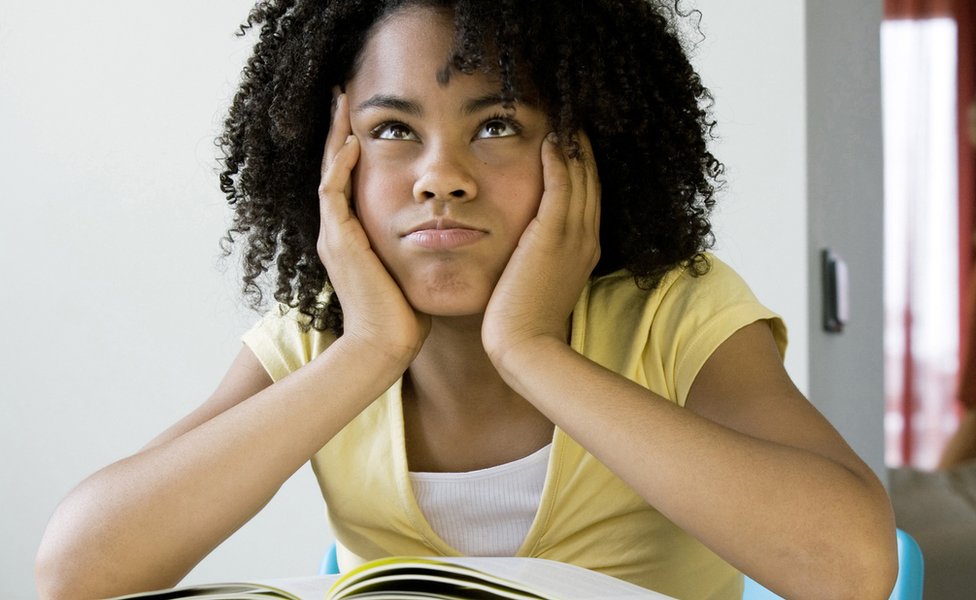 Девушка с афро сидит за столом с книгой