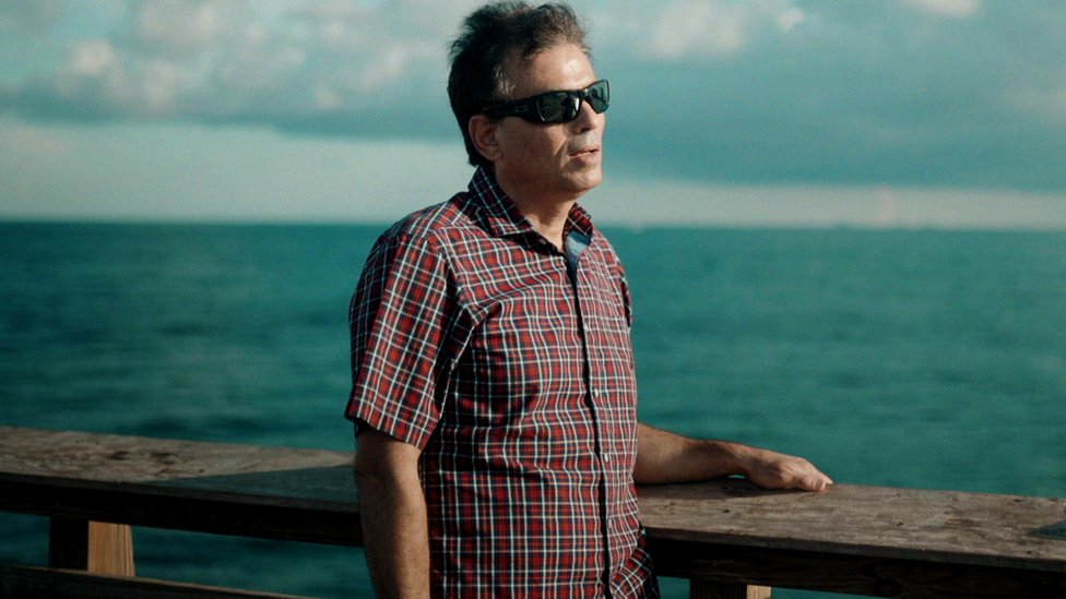 A portrait of Ahmed Faroukhi, wearing dark glasses, by the ocean