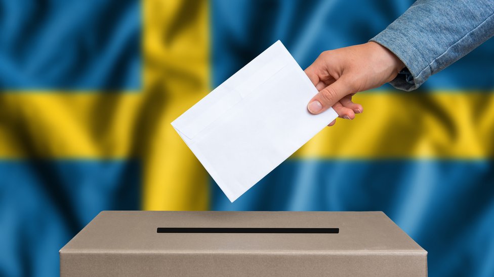 Urna de votación con bandera sueca de fondo.