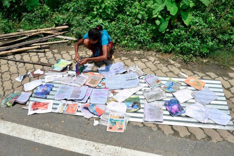 Девушка кладет свои школьные учебники сушиться вдоль дороги в пострадавшем от наводнения районе Хатишила в районе Камруп индийского штата Ассам 16 июля 2019 года.