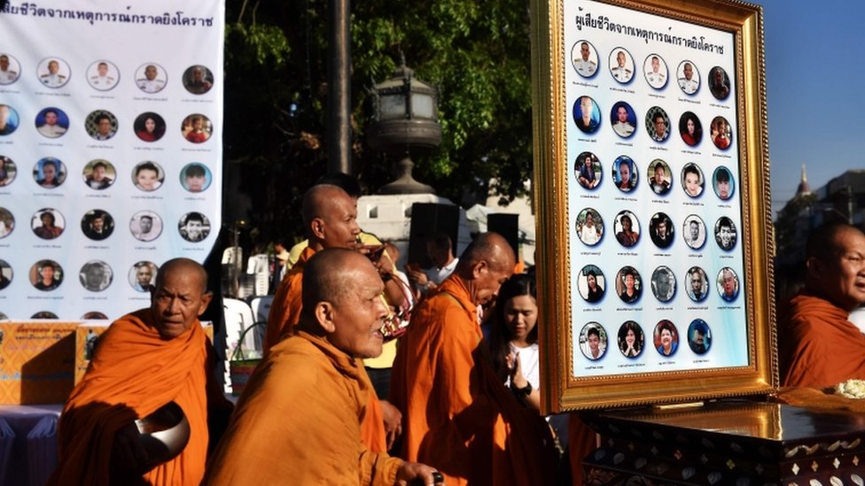 Буддийские монахи проходят мимо фотографий жертв массового расстрела через неделю после того, как одинокий солдат застрелил 29 человек в Таиланде