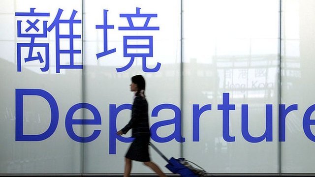 An airline steward in front of a departure gate sign in Chek Lap Kok airport, Hong Kong, 2003