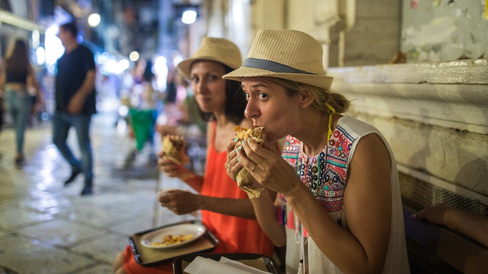 Duas turistas comendo sanduíche na rua