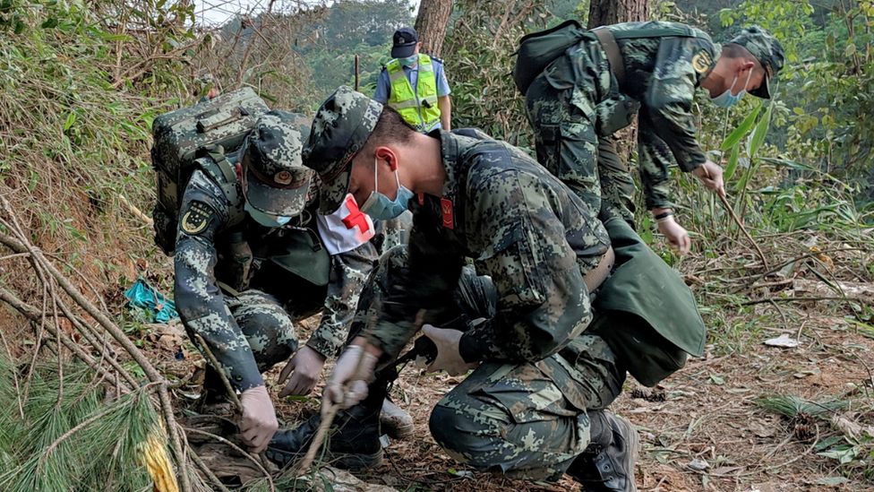 Soldiers in camouflage fatigues searching the forested hillside of the crash site