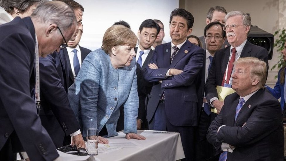 Líderes en el G7 mirando a Trump sentado.