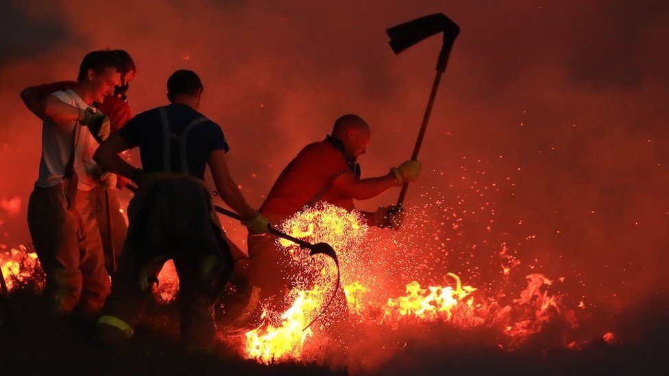 Bomberos combaten un incendio descontrolado con batidores en Winter Hill, cerca de Bolton, Reino Unido, el 28 de junio de 2018