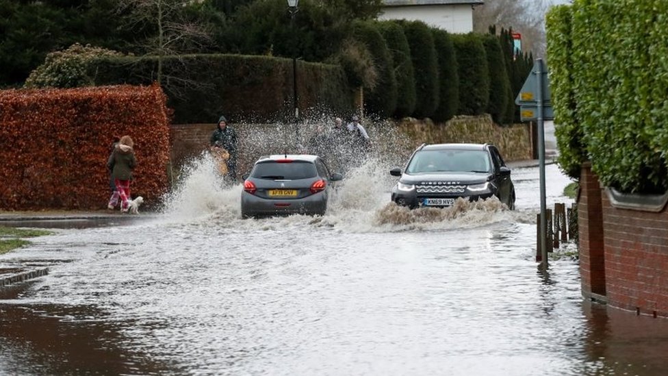 Cars drive through a flooded street in Great Barford, near Bedford,