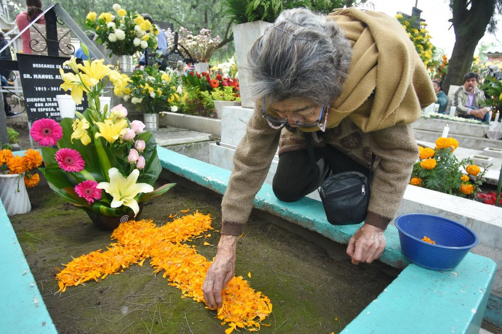 Mujer coloca flor de cempasúchil en una tumba.