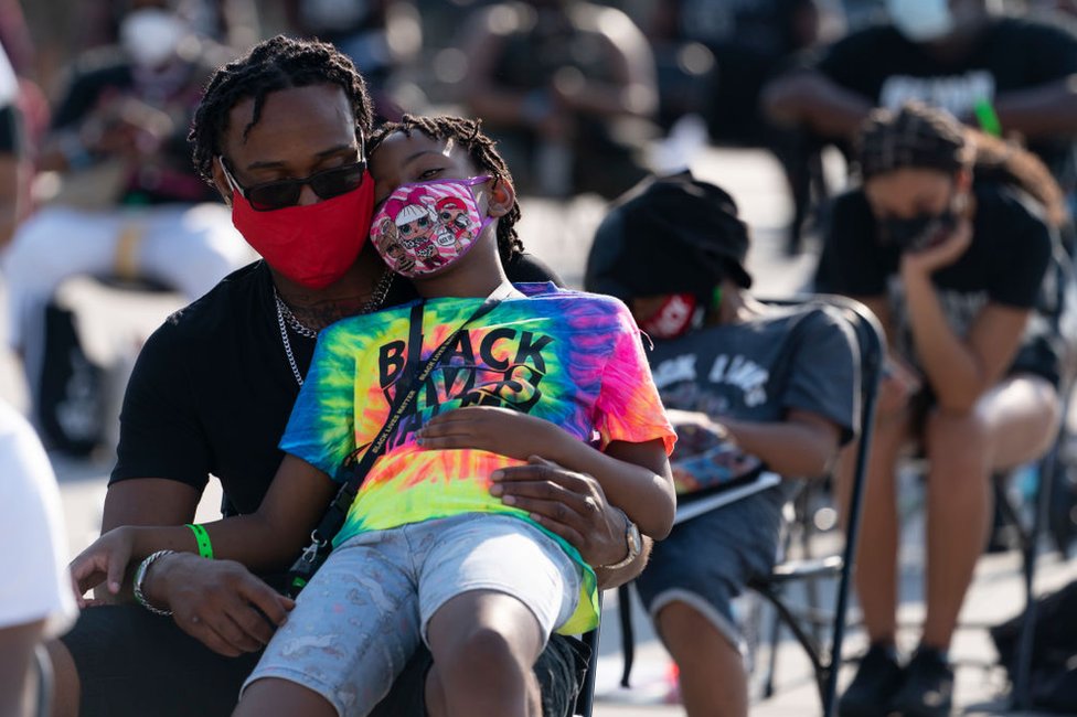 Marlon Holmes, de Chicago, con su hija Victoria Mone, de 8 años, en su regazo mientras esperan el inicio de una protesta contra el racismo y la brutalidad policial el 28 de agosto de 2020 en Washington.