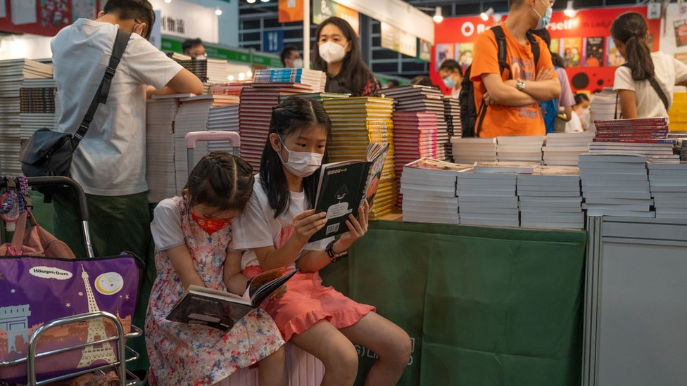 香港書展展場內一對小姊妹在一書攤前坐在行李箱上讀書（20/7/2022）