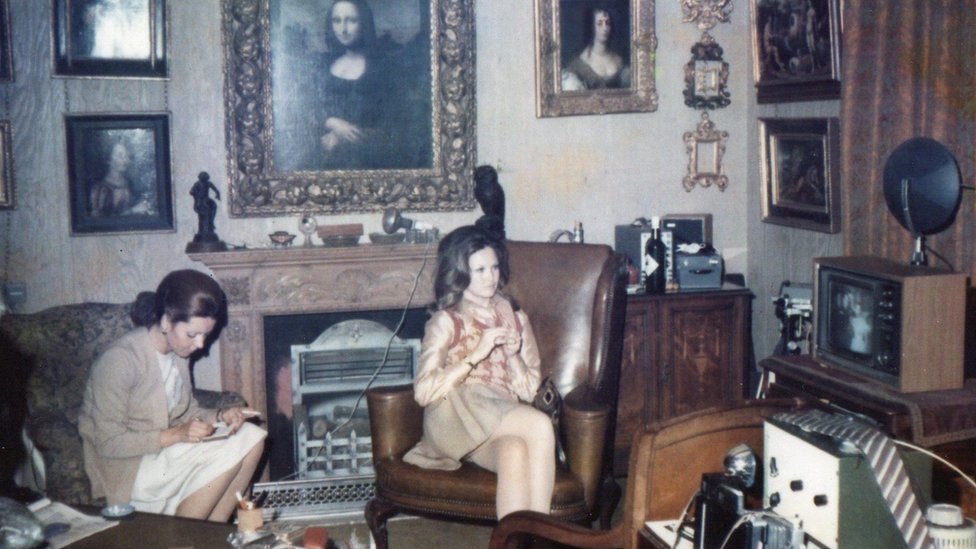 Two women sit beneath a Mona Lisa painting hanging above the fireplace of a 1960s London flat