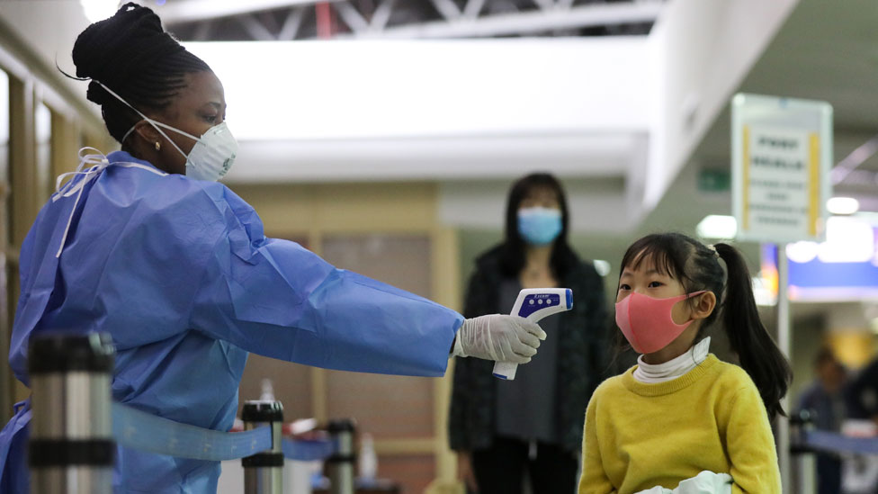 Кенийский медицинский работник (слева) проверяет пассажира в маске после того, как он прибыл из Китая, в международном аэропорту Джомо Кеньятта в Найроби, Кения, 29 января 2020 года
