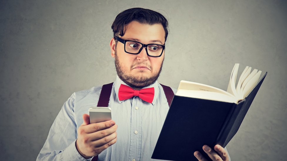 Hombre leyendo libro y usando celular