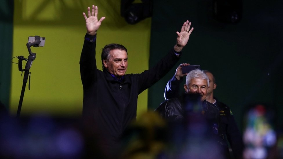 Bolsonaro acenando e sorrindo em cima do palco