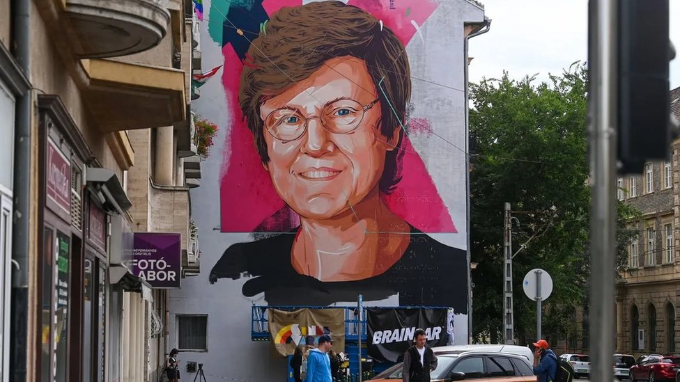 Mural na lateral de um prédio mostra o rosto da cientista Katalin Kariko, uma mulher branca de óculos e cabelo curto