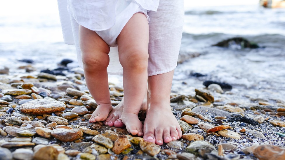 Los pies de una madre y su bebé dando pasos en la playa