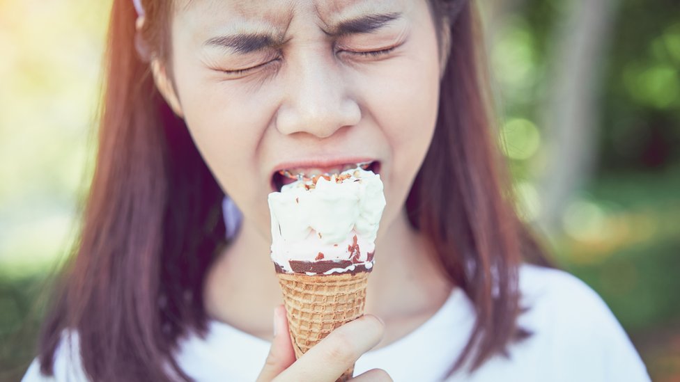 Una joven con expresión de dolor por comer helado