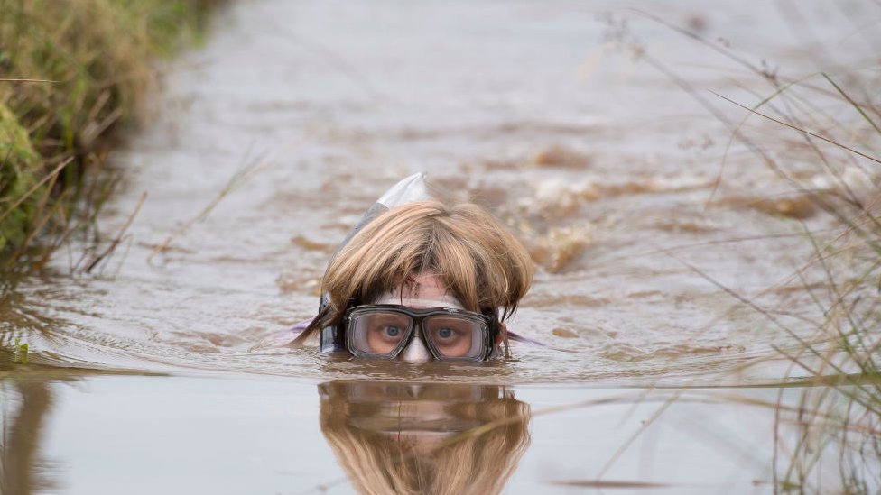 Женщина в очках и трубке частично погружена в воду, и только ее голова видна над водой