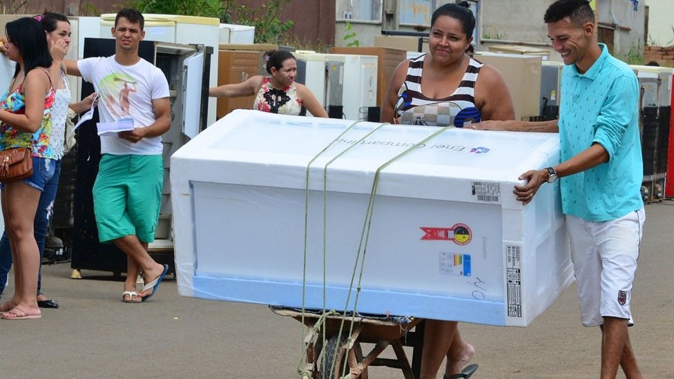 Mulher leva geladeira nova em carrinho de mão durante ação de distribuição